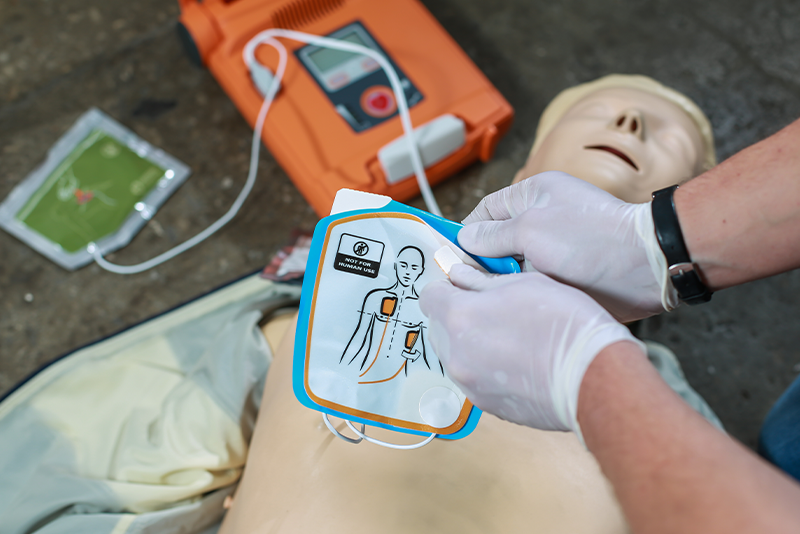 Two hands in nitrile gloves prepare and practice automated external defibulator or AED to be placed on a training dummy in a first aid class.