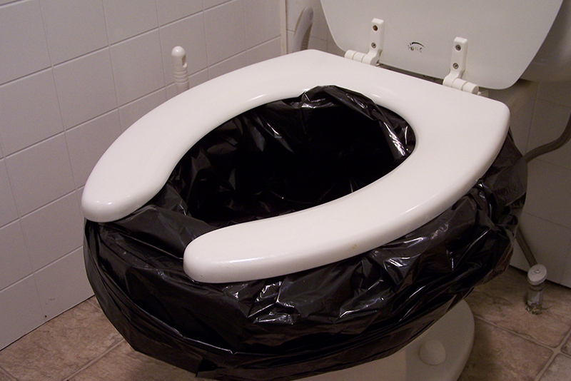 An elongated toilet with a black garbage bag lining the bowl.