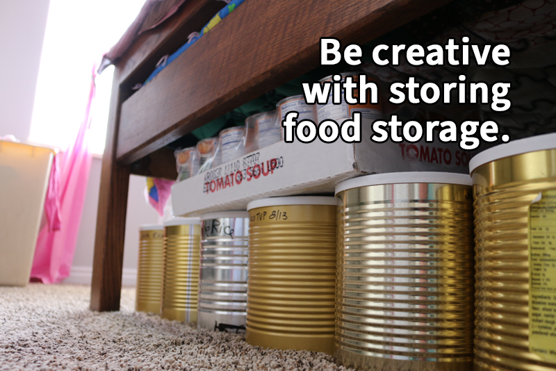 Cans of dry food stored under a bed. text reads, "Be creative with storing food storage."