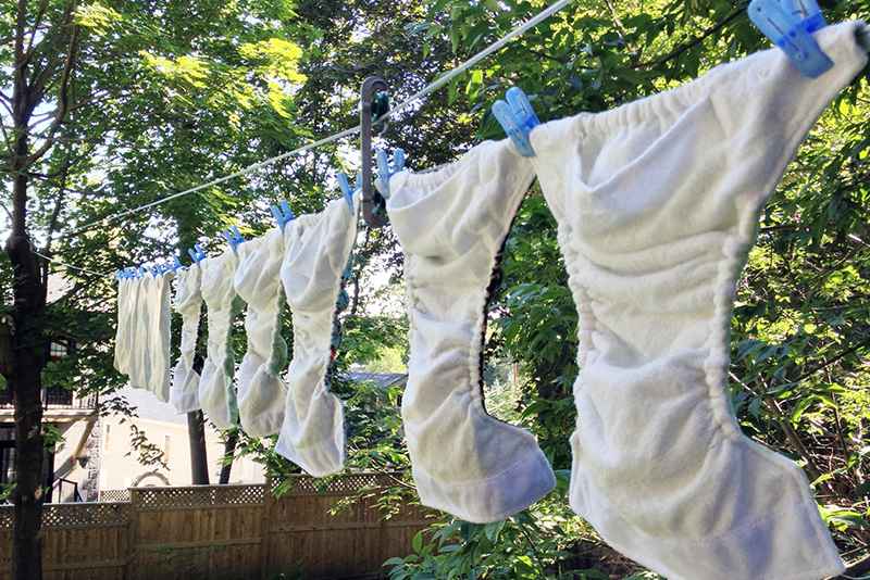 White cloth diapers hanging on a clothesline in a tree filled backyard.