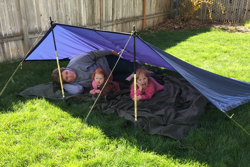 Happy woman and two young daughters in a lean-to tent in their backyard.