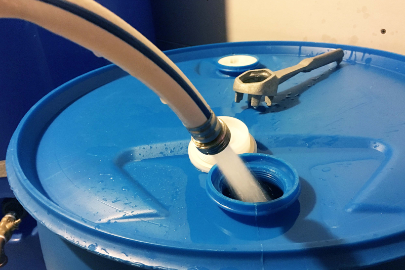 White drinking water hose being used to fill blue 55 gallon water barrel.