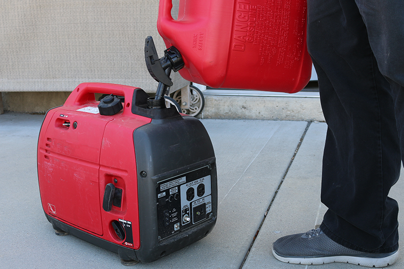 A man fills a 2000 watt generator on his backporch with a five gallon fuel can.