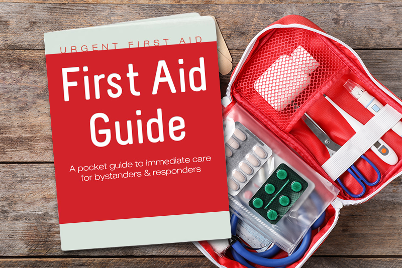 An open pocket-sized first aid kit sits open on a rough wooden table. In front of the kit is a booklet with the title, "First Aid Guide, A pocket guide to immediate care for bystanders and responders."