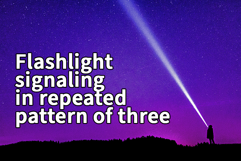 A person stands on a hill at night shining a bright flashlight beam into a star-filled purple sky with the text "Flashlight signaling in repeated pattern of three."