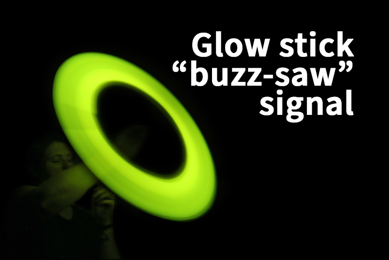 A person is spinning a green glow stick on a string creating a circular light pattern with the text "Glow stick 'buzz-saw' signal" displayed on a black background.