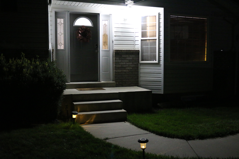 Front porch of a home in the dark. Porch light is on and lights line the path to the front door.
