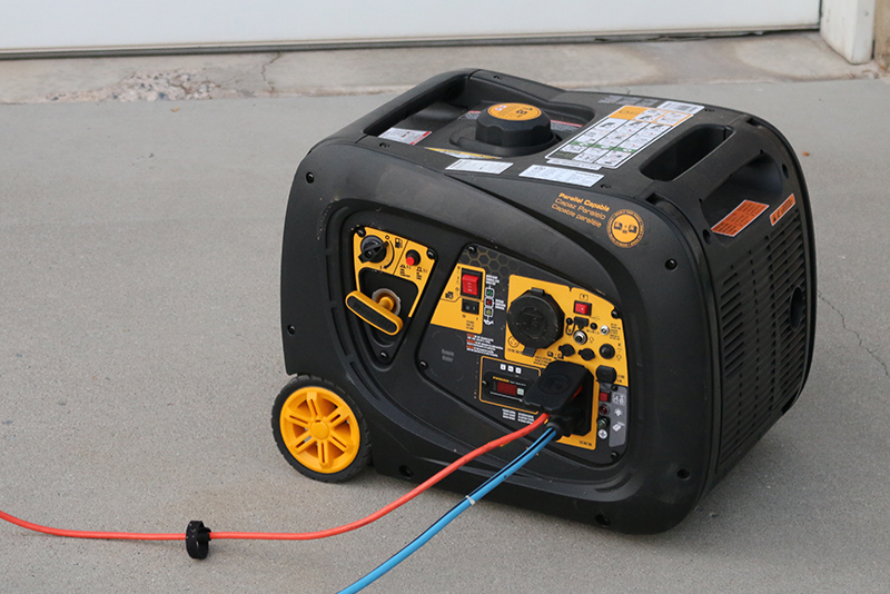 A portable 3000 watt generator sits on a driveway with two electrical cords plugged into it.