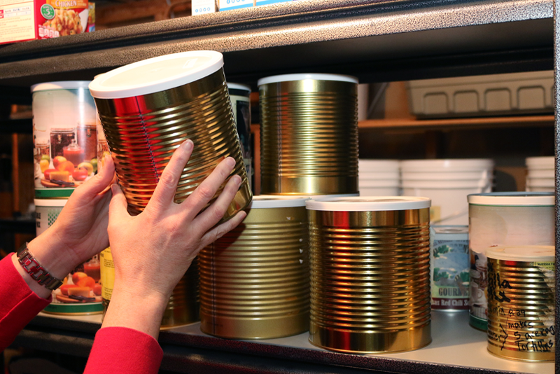 Woman pulling a large can of food off a shelf in a pantry.