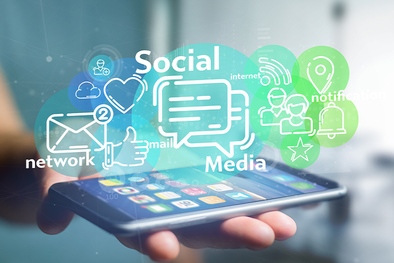 A hand is holding a smartphone with colorful social media and communication icons floating above the screen.