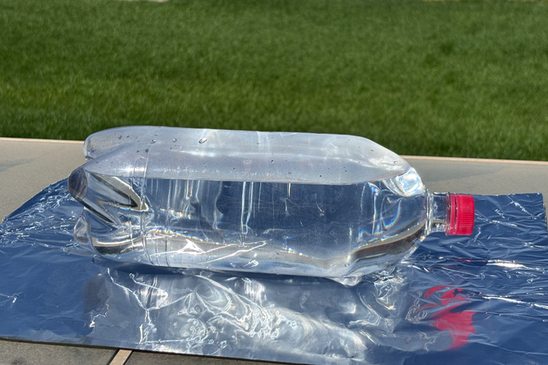 Two liter bottle laying on a sheet of aluminum foil in the outside sunshine.