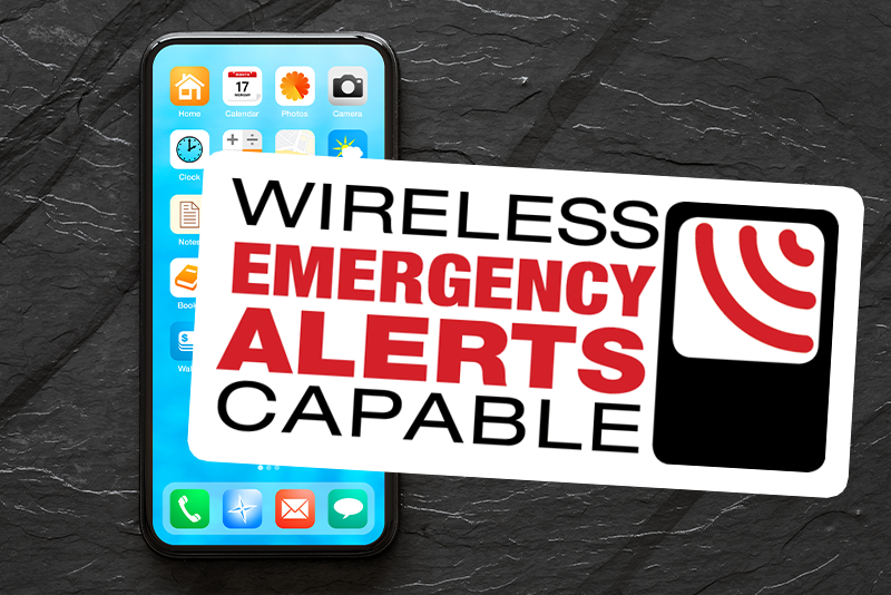 A logo with a mobile phone broadcasting a signal next to the words "Wireless Emergency Alerts Capable." This is the logo for WEA. The logo is in front of a smartphone on a black tabletop.