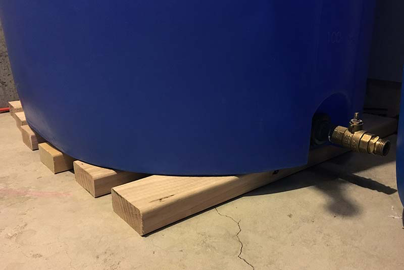 Blue water barrel on 2x4 boards, elevating it off of a concrete floor.