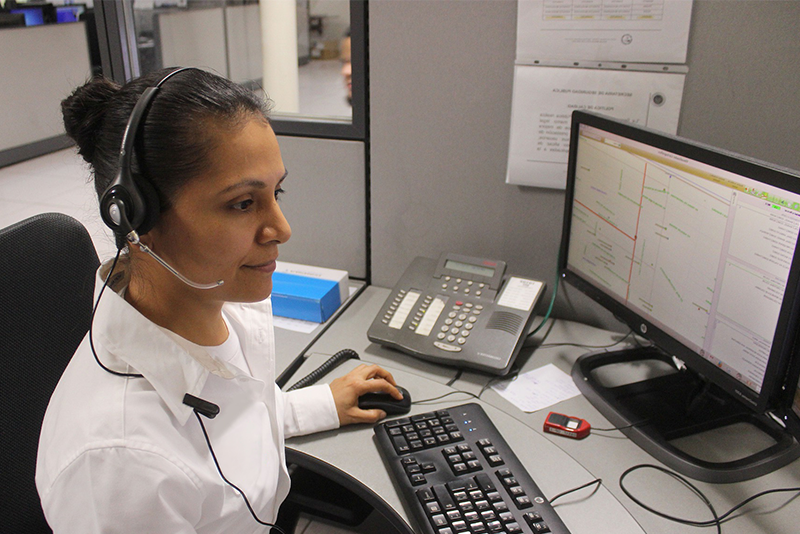 A woman dispater with a headset and microphone sits at a desk with a computer keyboard and two screens.